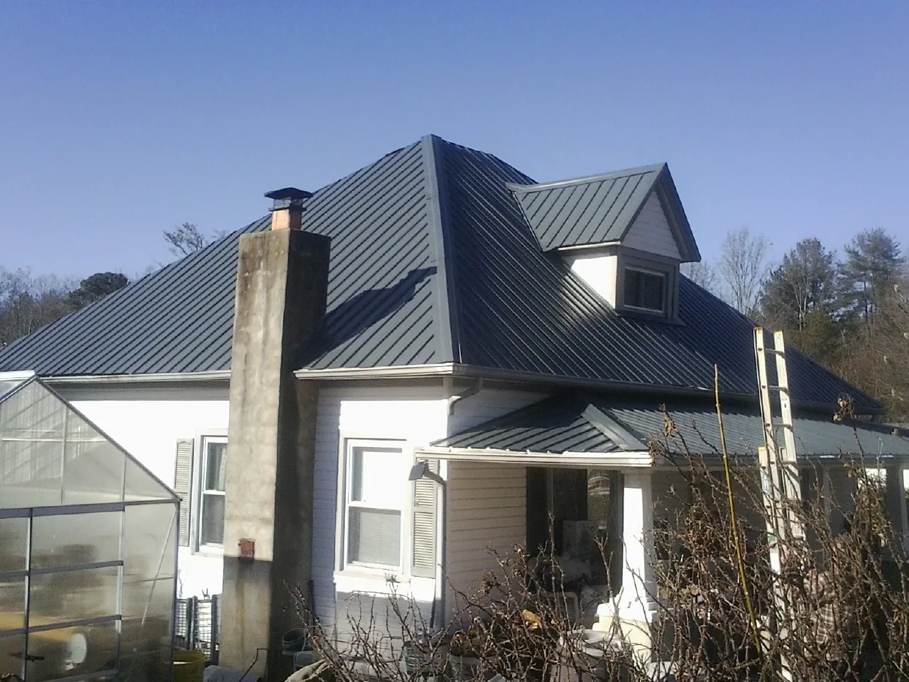 Dark blue standing seam metal roof on a white farmhouse with dormer — Slate & Tile Roof Repair by Roofing Brothers in Mableton