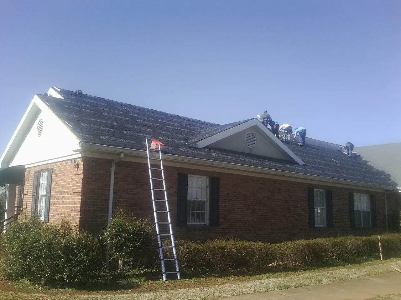 Crew tearing shingles off a brick ranch roof with a ladder set — Emergency Roof Repair work by our crew in Mableton