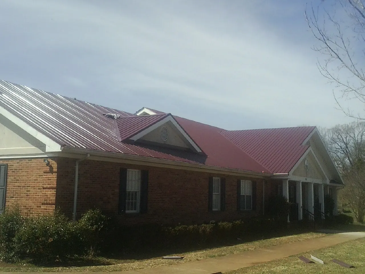 Red metal roof with gabled entries on a long brick building, from a Hail Damage Roof Repair job in Mableton