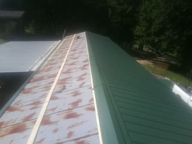Old rusted panels beside newly installed green metal roofing — Wind Damage Roof Repair by Roofing Brothers in Mableton
