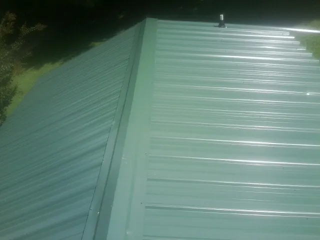 New green metal panels meeting at the ridge of a roof — Flat Roof Repair work by our crew in Mableton