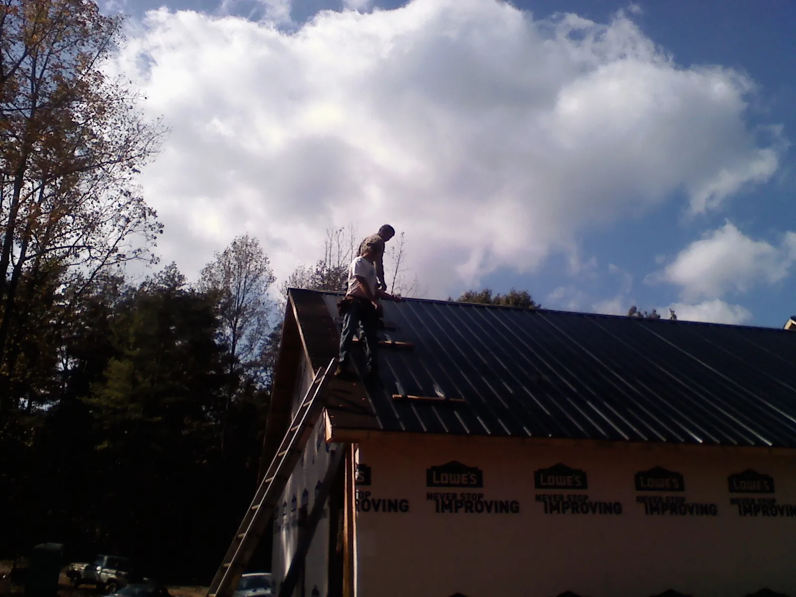 Roofer fastening dark metal panels high against a cloudy sky, from a Roof Inspection job in Mableton