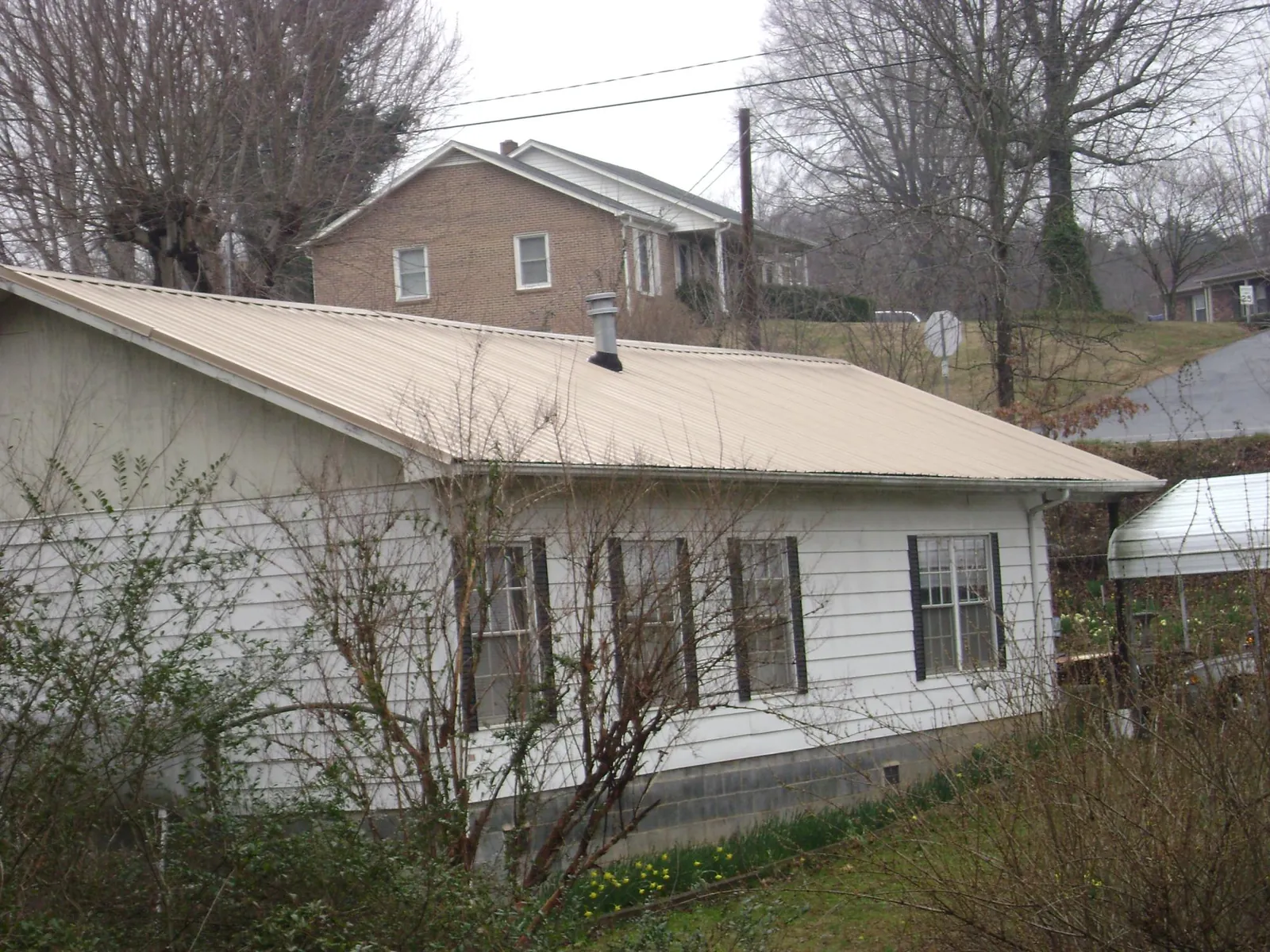 Tan metal roof on a white sided house set into a hillside — Commercial Roofing by Roofing Brothers in Mableton